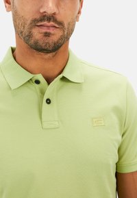 Polo shirt in lichtgroen, gemaakt van textuurstof. Beschikt over een klassieke kraag, een knoopsluiting met twee knopen en een klein geborduurd logo op de borst.