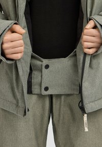 Groene geblokte jas met ritssluiting en drukknoopsluitingen, met een zwarte binnenvoering. Gepaard met bijpassende gestructureerde broek.