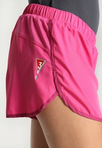 Pantalones cortos deportivos rosas hechos de una tela ligera con una cintura elástica, que cuenta con una abertura lateral y un parche de logo triangular.