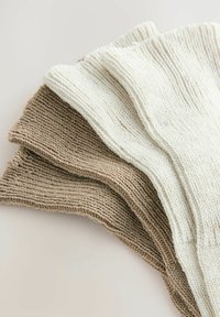 Pletená sveterová tkanina v béžových a bielych odtieňoch, s jemnou textúrou a rebrovaným dizajnom, uložená v preloženom usporiadaní.