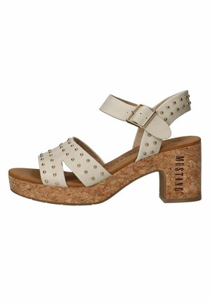 Beige open-toe sandaal met gouden studs, verstelbare enkelband en een stevige kurken hak met het merk "MUSTANG" aan de zijkant.