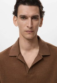 Brown knitted polo shirt with a perforated texture, featuring a structured collar, short sleeves, and subtle placket detail.