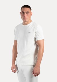 Hvid bomulds T-shirt med rund hals, korte ærmer og et lille logo på brystet. Simpelt design og blød tekstur.