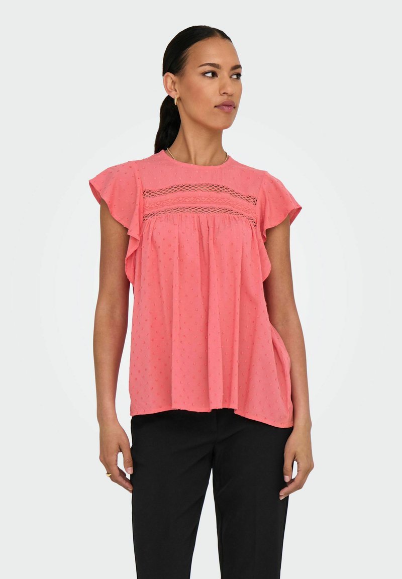 Blusa rosa intrecciata con maniche corte a volant, dettagli in pizzo decorativi sul petto e una vestibilità ampia. Tessuto morbido.