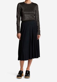 svart plisserad midikjol i kombination med en glittrig långärmad topp, med rund hals och texturerad tyg. Svarta träskor fulländar outfiten.