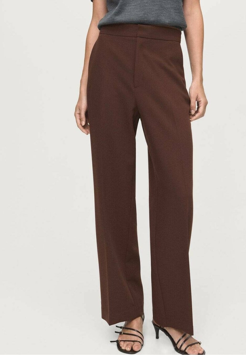 Femme portant un pantalon marron taille haute à jambes larges, associé à des sandales à talons noires à brides et un haut gris rentré.