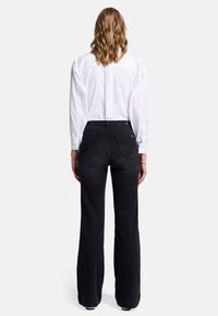 Black flared jeans with a high waist and subtle back pocket stitching details, paired with a white button-up shirt. Clean design, smooth texture.