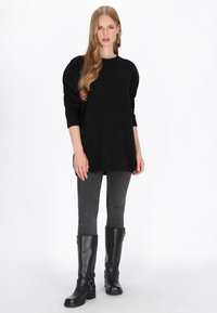 Fekete, oversize kötött pulóver kerek nyakkivágással, hosszú ujjakkal és oldalsó hasítékokkal, sötétszürke slim-fit farmerrel és térd fölé érő fekete csizmával párosítva.