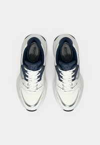 Λευκά αθλητικά παπούτσια με ναυτικές λεπτομέρειες, υφασμάτινη επιφάνεια με υφή, γυαλιστερό ασημένιο περίβλημα και εσωτερική επένδυση με σχέδιο. Τα κορδόνια είναι λευκά και επίπεδα.