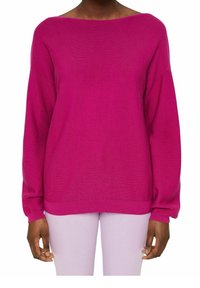 Personne portant un pull à manches longues rose vif avec un large col bateau et un pantalon ajusté lavande clair.