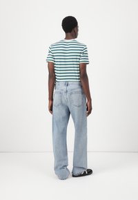 Striped green and white short-sleeve shirt, relaxed fit, paired with light blue wide-leg jeans. Black sandals detail the feet.