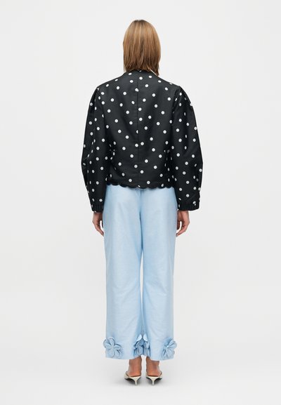 Juoda striukė su baltomis taškeliais, su banguotu apačios kraštu, derinama su šviesiai mėlynomis platėjančiomis kelnėmis, kurių apačioje yra gėlių raštai.