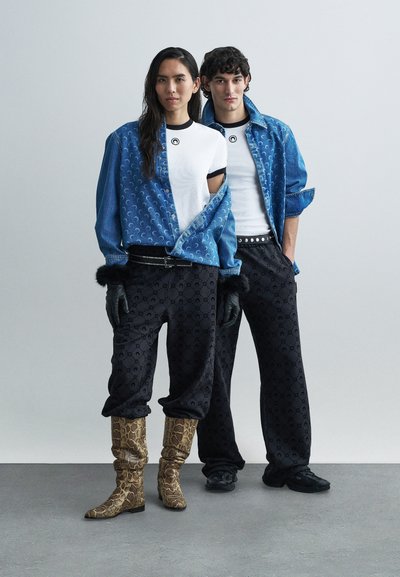 Denimtakki kuvioiduilla paneeleilla, valkoiset t-paidat, mustat kuvioidut housut ja käärmekuvioiset saappaat. Mukana hansikkaat ja hopeiset yksityiskohdat sisältävä vyö.