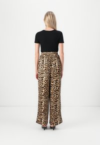 Svart kortermet topp kombinert med vide bukser i leopardmønster med elastisk midje og glatt, glansfullt stoff.