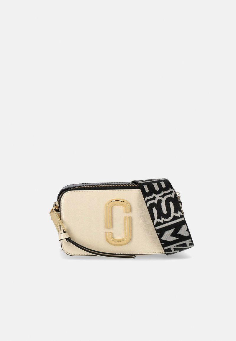 Torebka typu crossbody w kolorze beżowym z złotymi akcentami, zamykana na zamek, z czarnym wzorzystym paskiem i wyraźnym logo z przodu. Gładka faktura.