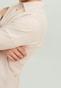 Vaaleanpunainen nappipaita, jossa on teksturoitu kangas, taitettava kaulus ja yksi nappikiinnitys kaulassa. Slim fit -leikkaus, jossa on näkyviä ompeluseikkoja.