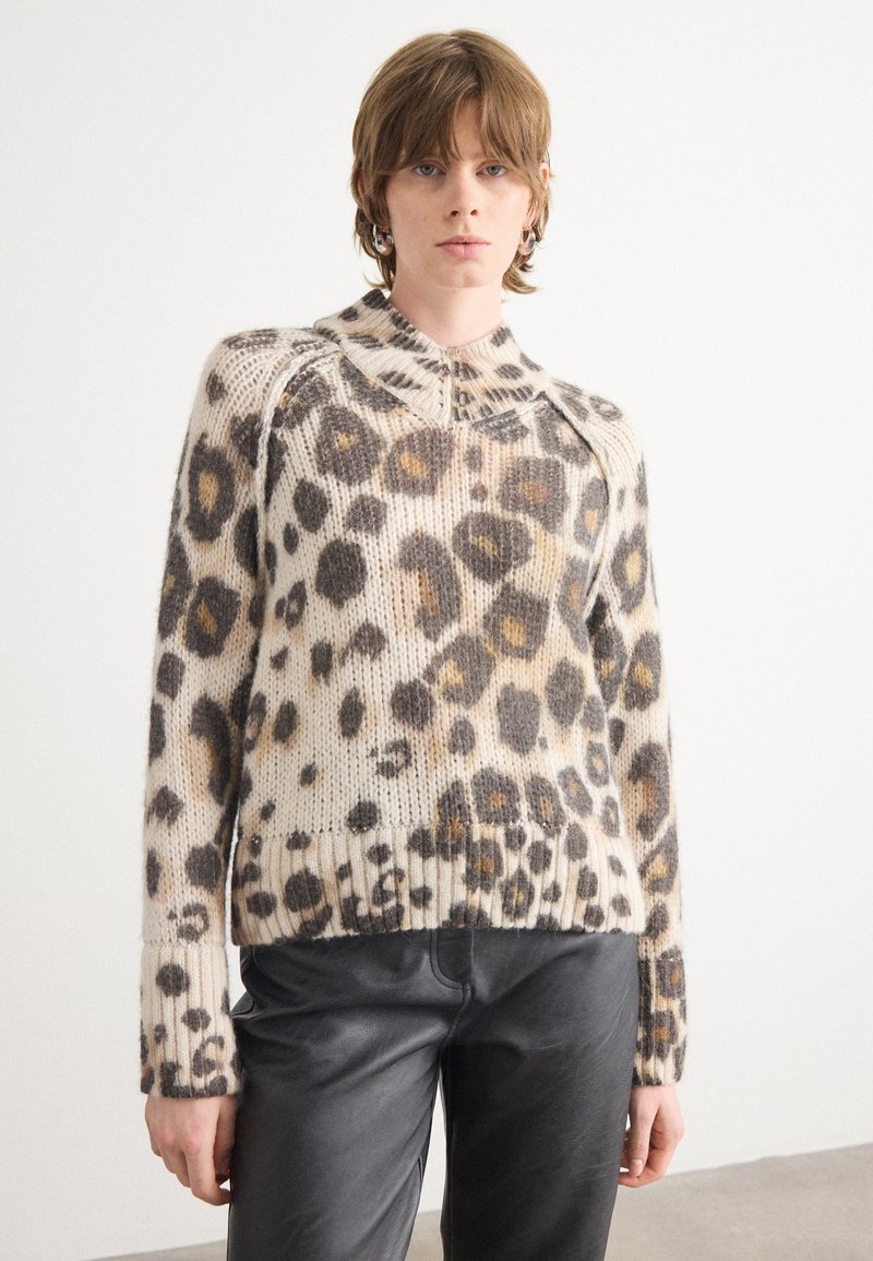 Pull en imprimé léopard dans des tons beige et marron, avec des poignets et un ourlet côtelés, col rond avec un détail zippé. Porté avec un pantalon noir.