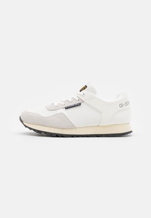 Baskets basses blanches et beiges avec des panneaux en mesh et en daim, étiquette logo G-Star Raw noire, et semelle en caoutchouc noire avec une adhérence texturée.