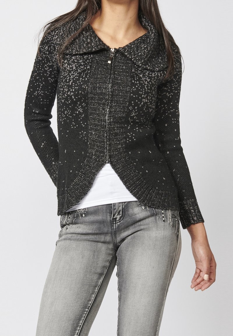 Black knit cardigan with a textured pattern, featuring a wide collar and asymmetrical hem. Zipper closure, long sleeves, and slight sparkle detailing.