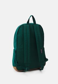 Green fabric backpack with adjustable straps, a textured back, and brown base. Features a top handle and side pocket. No visible logos.