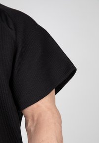 Zwarte textuur top met een losse pasvorm en brede, korte mouwen, die een subtiel ruitpatroon op een zachte stof benadrukt.