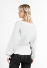 Suéter de punto suelto gris claro con un amplio escote, dobladillo acanalado y mangas cortas; combinado con pantalones negros ajustados.
