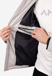 Chaqueta gris ligera con forro negro, que cuenta con un bolsillo interior con cremallera y un puño ajustable en la manga.