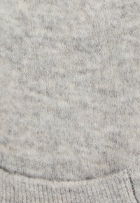 Tessuto di maglione grigio chiaro con un motivo tessuto testurizzato. Il materiale appare morbido con una superficie leggermente pelosa e un orlo a coste.