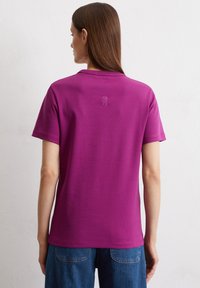 Tegelijkertijd paars T-shirt met korte mouwen, een gladde textuur en een klein geborduurd logo op de achterkant, gecombineerd met blauwe denim broek.
