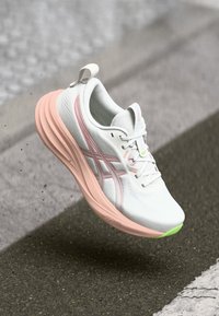 White athletic shoe with pink and green accents, textured mesh upper, cushioned sole, and traditional lacing system.