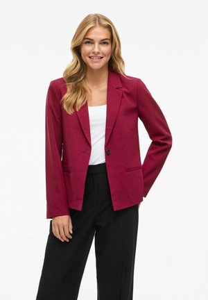 Burgundský tailored blejzr s jedním knoflíkem, klopami a dvěma předními kapsami; nošený s bílým topem a černými kalhotami.
