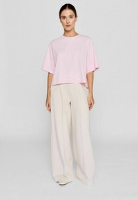 Pink cropped t-shirt with wide short sleeves, paired with cream wide-leg trousers featuring front pleats and a smooth texture.