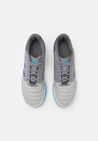 Grå sportskor med syntetiskt övre, vadderad krage, blå accenter, texturerat tåskydd och gummisulor. Skosnören i matchande grå.