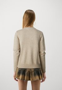 Beige stickad tröja med ribbad fåll och ärmslut, med en enkel rund halsringning. Kombinerad med en svart och brun ombré plisserad kjol.