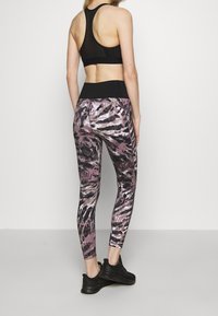 Zwarte atletische tanktop gecombineerd met kleurrijke, gebloemde leggings met roze, wit en zwarte abstracte ontwerpen. Zwarte sneakers.