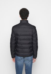 Black puffer jacket with a high collar, horizontal stitching, and a smooth texture. Paired with blue jeans, viewed from the back.