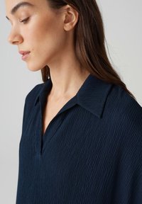 Camicia blu navy con finitura texture, caratterizzata da un colletto a revers e una vestibilità comoda. Il tessuto leggermente sgualcito aggiunge profondità.