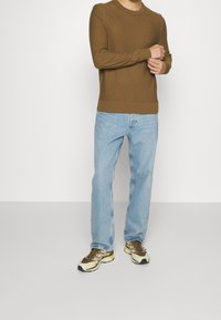 Pull en tricot marron avec col rond, associé à un jean bleu clair droit et des baskets marron et jaune. Design simple et coupe décontractée.