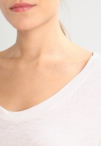 Valkoinen, kevyt, lyhythihainen toppi, jossa on leveä V-pääntie ja pehmeä rakenne, joka sisältää hienovaraisia vaihteluita kankaan paksuudessa.