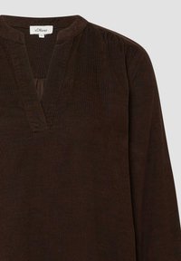 Bruine corduroy top met een V-hals, lange mouwen en geplooide details op de schouders. De textuur is geribbeld, wat zorgt voor een subtiel patroon.