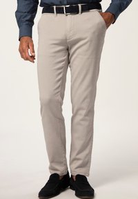 Chinos beige claro fabricados en algodón suave, con un corte ajustado, bolsillos laterales y una textura suave, acompañados de un cinturón oscuro y zapatos negros.