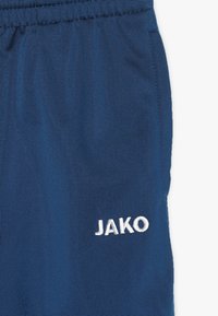 Marineblaue Sportshorts aus strukturiertem Stoff, mit elastischem Bund und weiß gesticktem "JAKO"-Logo auf der linken Seite.