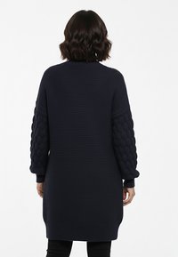 Sweter kardigan w kolorze granatowym z teksturowanymi, pęcherzykowatymi rękawami, długim krojem i prążkowanymi mankietami. Miękki, gruby materiał o pudełkowej sylwetce.