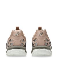 Beige sport schoenen met een achterste trekband, mesh accenten en een grijzige zool. Zijpanelen hebben een gelaagd patroon en een dempende detail.