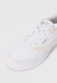 White athletic shoe with a textured synthetic upper, featuring a light beige accent and a lace-up design. Rubber outsole visible.
