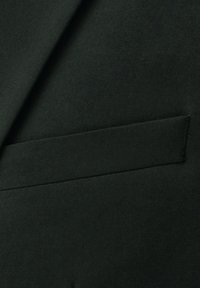 Schwarzer Anzugsstoff mit glatter Textur. Verfügt über eine rechteckige Brusttasche mit sauber genähtem Rand.