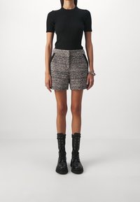 Svart ribbad kortärmad topp i kombination med grå och svart tweed-byxor med struktur som har sidofickor, buren med knähöga svarta snörstövlar.