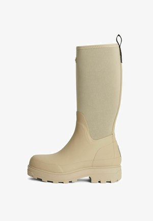 Beige vattentäta gummistövlar med en slät yta, texturerat nedre område och en dragöppning på baksidan för enkel påtagning. Midja-höjd.