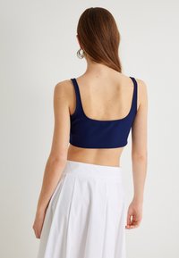 Marineblå cropped top med brede stropper og udrundet ryg. Glat stof med minimale sømme, parret med en hvid plisseret nederdel.