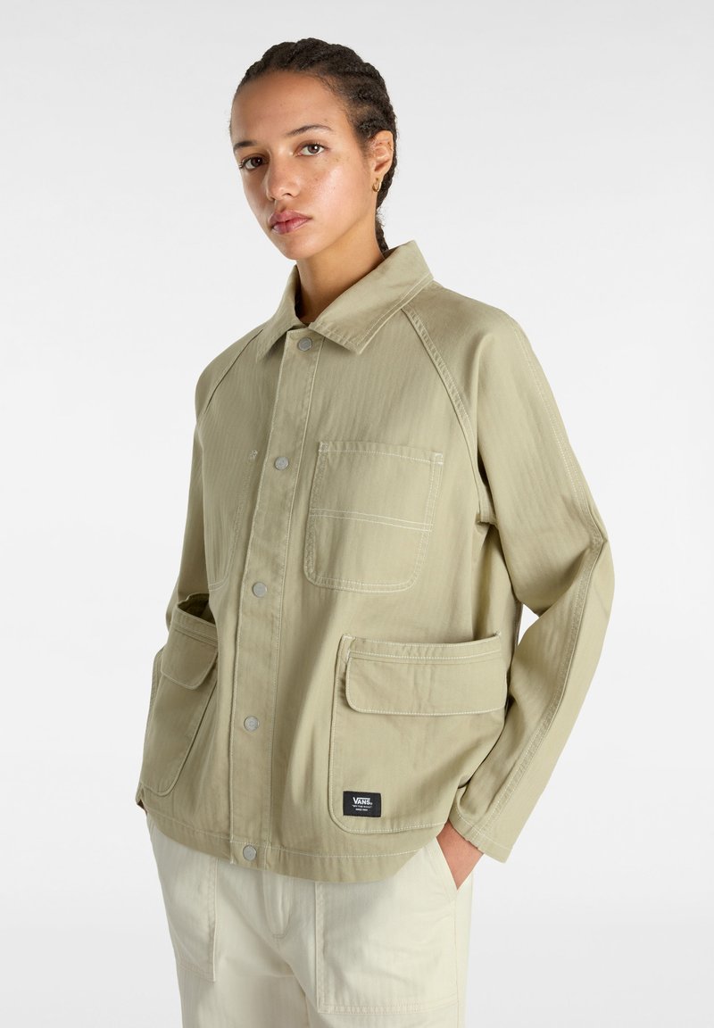 Chaqueta de un verde oliva claro con cuello, dos bolsillos frontales y un pequeño parche con logo. Hecha de un tejido texturado con costuras visibles.